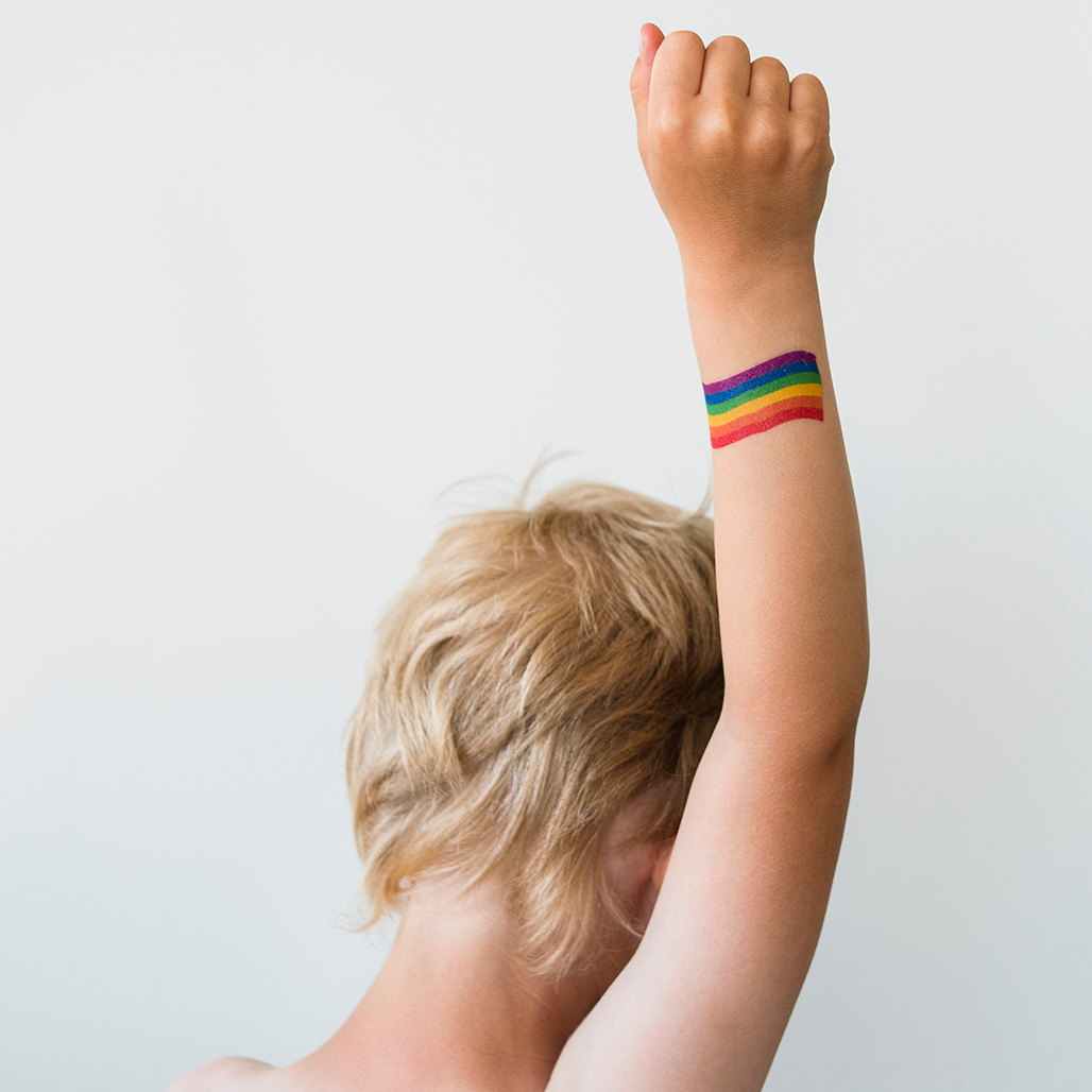 Pojke som höjer sin näve med regnbågsflagga ritad på armen