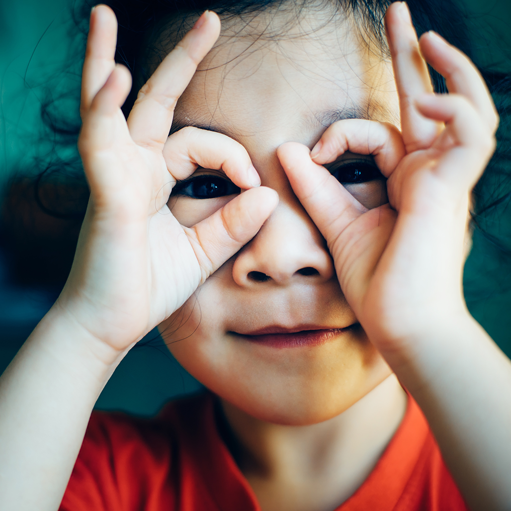 Flicka som gör en kikare med sina händer och tittar ut genom dessa