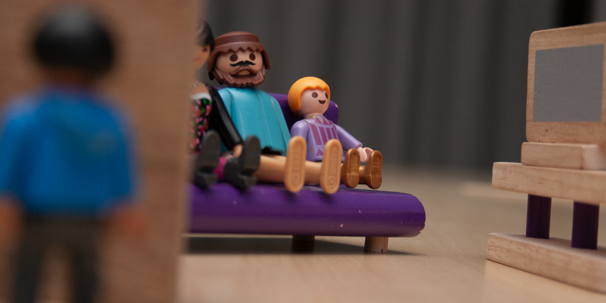 Bild på Playmobil-dockor. En familj som tittar på TV och en pojke som står utanför.