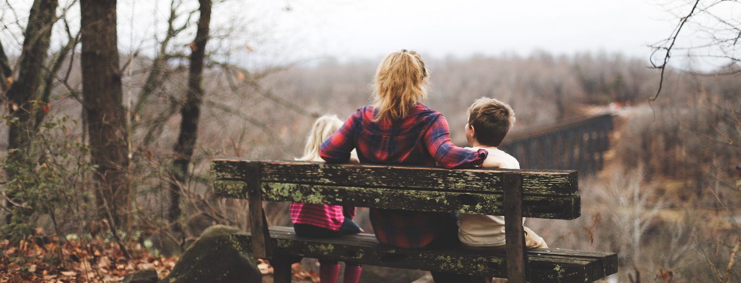 Mamma och två barn sitter på en bänk.