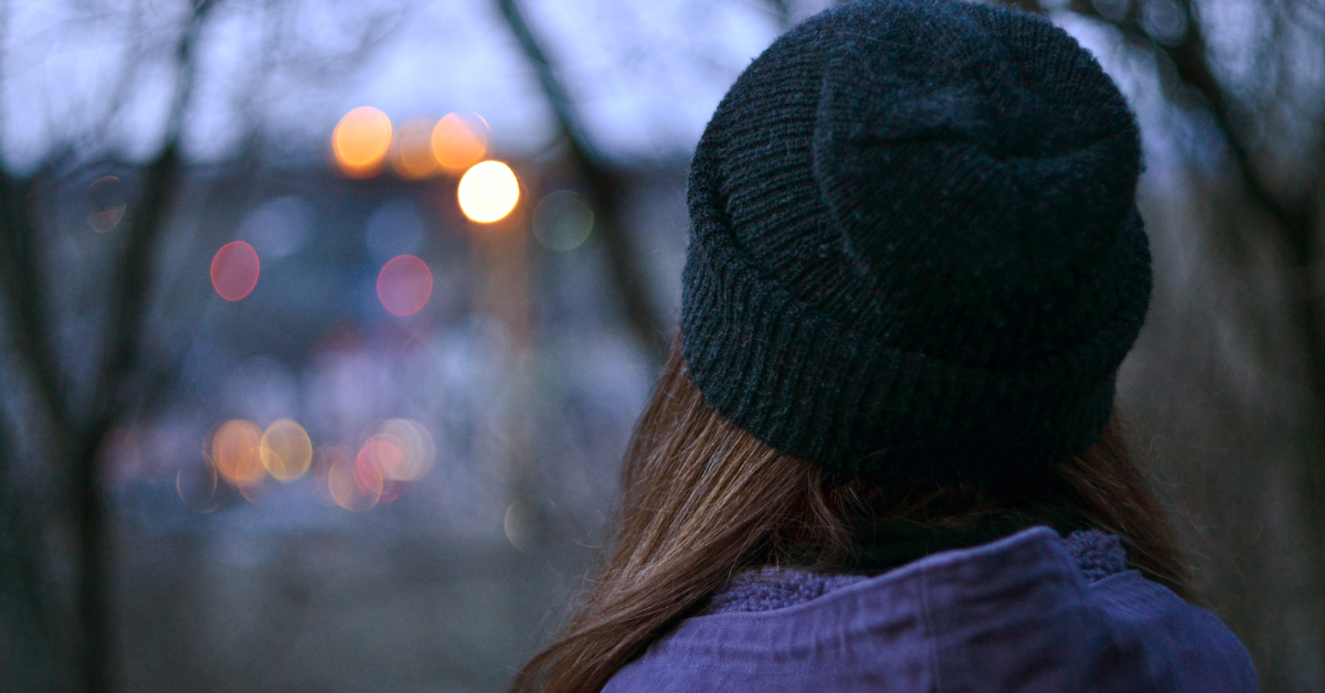 Bild på en flickas rygg. Flickan har mössa och tittar ut över vatten.